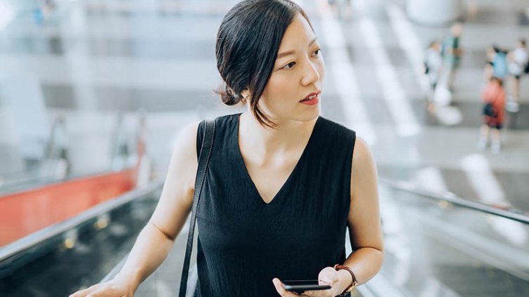 A woman holding mobile while standing in Escalator