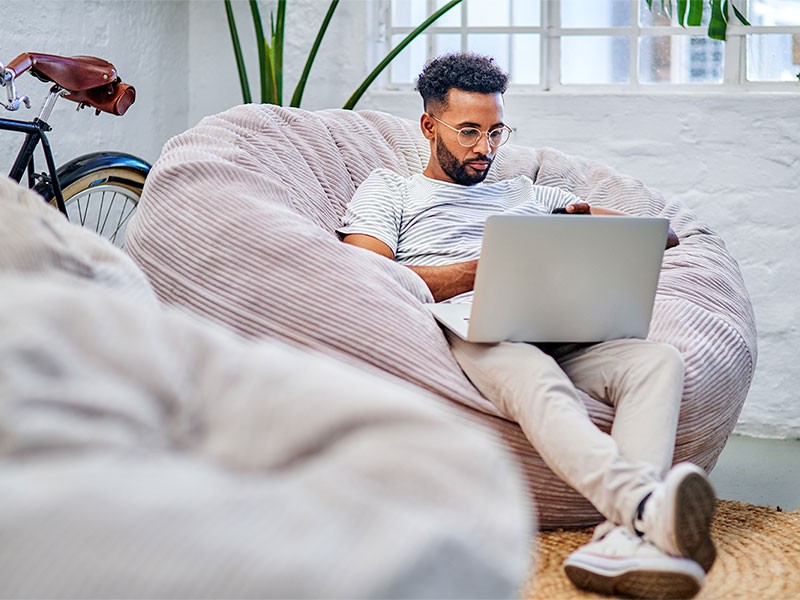 Man sat on cushion, working on his laptop.