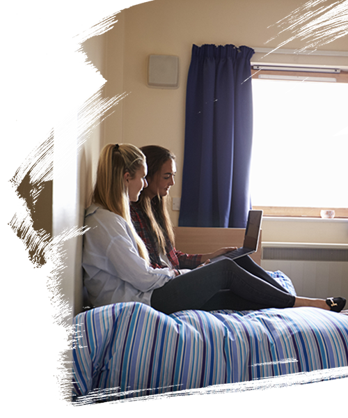 2 students sitting at student housing and discussing while looking at laptop